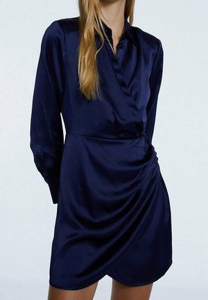 Abito in satin blu navy con design avvolgente, maniche lunghe e colletto a bottoni. Presenta dettagli drappeggiati in vita per una maggiore texture.