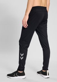 Zwarte sportbroek met een taps toelopend ontwerp, een elastische tailleband en reflecterende chevron details op het onderbeen. Gemaakt van lichtgewicht stof.
