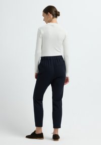 Marineblauwe broek met een taps toelopende pasvorm en elastische tailleband, gecombineerd met een witte geribde lange mouwen top en donkere schoenen.