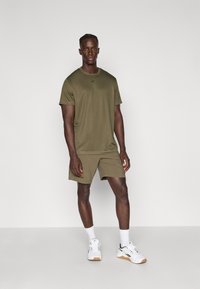 Olíva zöld sportos öltözet, amely egy rövid ujjú pólóból és sortból áll, lélegző anyagból készült, laza fazonú és egyszerű dizájnnal.