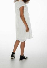 Robe blanche longueur genou avec manches courtes, présentant des détails texturés et une coupe ample, associée à des baskets montantes noires.