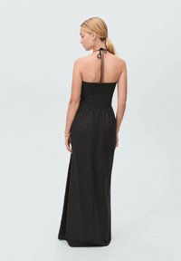 Black maxi dress with a smocked bodice, halter neck tie, and a textured pattern. The design has a relaxed flow and falls to the ankles.