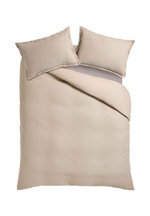 Housse de couette beige texturée avec deux taies d’oreiller assorties sur un lit, un coin de la couette légèrement replié.
