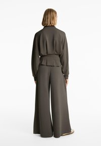 Oversized dark green sweatshirt with a high collar, pleated back detail, paired with wide-legged matching trousers. Soft texture and relaxed fit.