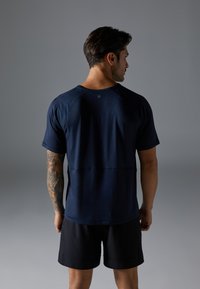 Navyblaues Sport-T-Shirt mit kurzen Ärmeln und Rundhalsausschnitt, aus glattem Stoff gefertigt. Hat ein dezentes Logo auf der Rückseite und wird mit schwarzen Shorts kombiniert.