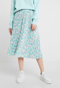 Plisserad midi kjol i en ljusgrön färg med ett blommönster i rosa och blått. Stylar med vita sneakers och en ljusblå tröja.