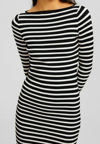 Abito a righe bianche e nere con maniche lunghe e scollatura a barca, caratterizzato da una silhouette aderente e un tessuto texturizzato.