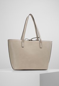 Beige kožená taška přes rameno s dvěma popruhy, minimalistický design, kontrastní černé okraje a měkká, hladká textura.