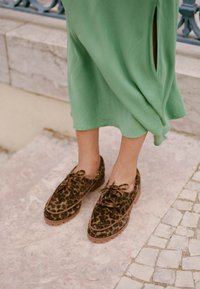 Hnědé boty s leopardím vzorem a jemnou texturou, s šněrováním a nízkou plochou podrážkou. Nosené s zelenými šaty, které mají boční rozparek.