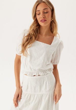 Witte katoenen blouse met korte pofmouwen en vierkante halslijn, voorzien van bloemige oogjespatronen en een gerimpelde zoom. Draag met een bijpassende rok.