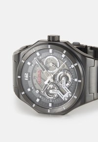 Black stainless steel watch with a multi-layered dial, silver accents, date function, and bold hour markers. Features a textured band.