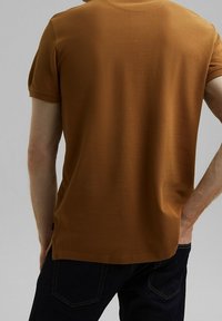 T-shirt marron à manches courtes avec une finition texturée. Il présente un col rond et une coupe droite, associé à un jean foncé.
