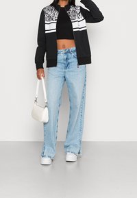 Chaqueta bomber en blanco y negro con un patrón de cebra en la parte superior, combinada con jeans de pierna ancha en azul claro y zapatillas de plataforma blancas. Bolso blanco.