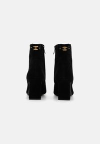 Botines de ante negro con tacón cuadrado, detalles en dorado y una cremallera en la parte trasera. Textura suave con un diseño elegante.