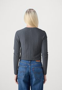 Sivi strukturirani dugoročni top s okruglim izrezom, uparen s plavim trapericama koje imaju strašnje džepove i detalj od kože.