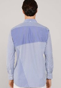 Camicia a righe con maniche lunghe, righe verticali blu e bianche, tessuto blu a contrasto sulla parte superiore della schiena, vestibilità sartoriale.