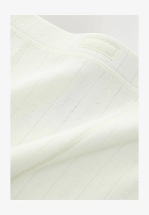 Biely pletený textil s vertikálnym ryhovaním a malými diamantovými vzormi. Má mäkkú textúru a v rohu sa nachádza štítok označený "NEXT".