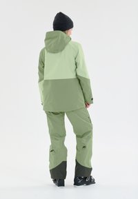 Vesivaton kahdesta osasta koostuva asu vaaleanvihreänä ja tummanvihreänä. Siinä on huppujakku, jossa on väri-erottelusuunnittelu, sekä löysät, kapenevat housut.