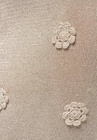 Tissu tricoté beige avec trois motifs brodés en forme de fleurs disposés de manière inégale sur la surface.