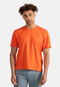 T-shirt di cotone arancione con scollatura rotonda e maniche corte. Piccolo logo grigio sul petto. Tessuto liscio, vestibilità rilassata.