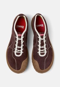 Brown suede sneakers with white laces and red insoles, featuring a flexible sole. Displayed from above on a white background.