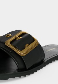 Μαύρο σανδάλι slide με φαρδιά λουρί που διαθέτει μεγάλη υφή με χρυσή αγκράφα και ραβδωτή μαύρη σόλα.