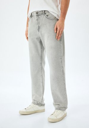 Light grey denim jeans with a relaxed fit, featuring five pockets, a button closure, and subtle fading on the fabric. Paired with white sneakers.