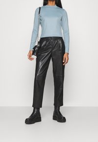 Maglia a maniche lunghe azzurro chiaro con colletto a coste, abbinata a pantaloni in pelle neri a vita alta e stivali neri con lacci spessi. Borsa nera.
