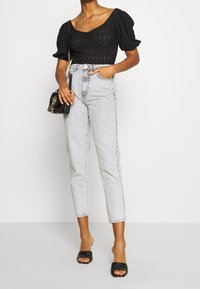 Černý pletený crop top s nafouknutými rukávy, světle šedé džíny s vysokým pasem a černé klouzavé sandály. Malá černá kabelka s řetízkovým detalem.