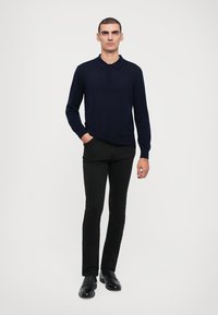 Polo din bumbac cu mânecă lungă de culoare bleumarin, cu un guler clasic, asortat cu pantaloni negri slim-fit și mocasini negri. Textură netedă, design ajustat.