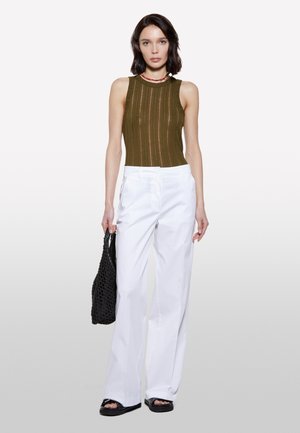 Top a costine verde oliva con scollatura tonda, abbinato a pantaloni bianchi a gamba larga e sandali neri con suola spessa. Gli accessori includono una borsa intrecciata nera.