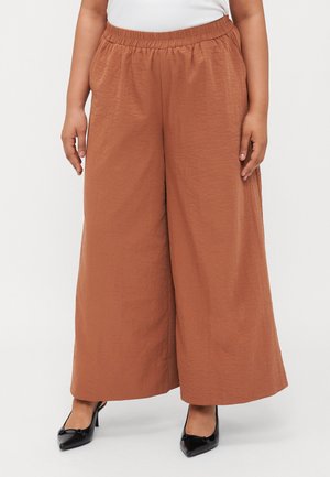 Brown wide-leg trousers made from textured fabric with an elastic waistband, paired with black pointed-toe heels.