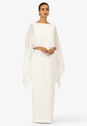 Langes weißes Kleid mit geradem Schnitt, das eine geschichtete, durchsichtige Cape über den Schultern und einen Boat-Neck-Ausschnitt hat. Glatte Textur.