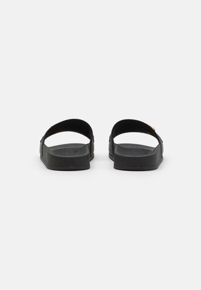 Schwarze Sandalen mit einem minimalistischen Design, breiten Riemen, einer strukturierten Fußsohle und einer flachen Sohle. Metallisches Detail neben dem Riemen.