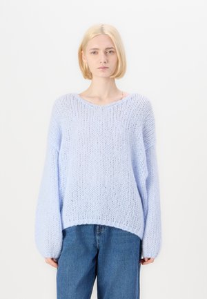 Maglione in maglia pelosa di un azzurro chiaro, con una vestibilità ampia, maniche larghe e orlo a coste, abbinato a jeans di denim. Texture morbida e aspetto vellutato.