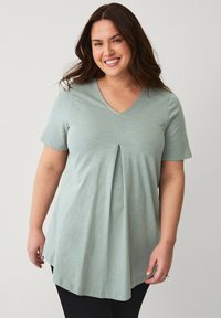 Lys grøn V-hals t-shirt med korte ærmer, der har en frontplysdetail og en afslappet pasform, lavet af blødt, struktureret stof.
