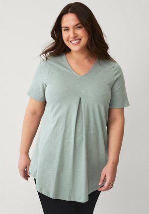 Jasnozielona koszulka V-neck z krótkim rękawem, z detalem w postaci fałdy na froncie i luźnym krojem, wykonana z miękkiego, teksturowanego materiału.
