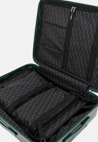 Valigia rigida verde con interno nero zipato, dotata di numerose tasche e divisori con zip, tutti decorati con un motivo a logo ripetuto.