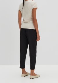 Ljusbeige kortärmad topp med ribbad textur, kombinerad med svarta tapered byxor med sidoklyftor och beige platta skor.