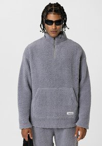 Fleece pullover in lichtgrijs, met een hoge kraag, kwartrits, kenguruzak en een gestructureerd, donzig materiaal.