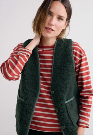 Grüne Fleece-Weste mit einer strukturierten Oberfläche, ausgestattet mit einem Knopfverschluss und zwei Taschen. Wird über einem rot-weiß gestreiften Langarmshirt getragen.