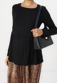 Svart långärmad topp med en figurnära bodice och utsvängd fåll, parat med byxor med leopardmönster och vida ben. En svart handväska fulländar looken.