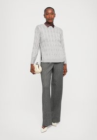 Light gray cable-knit sweater with long sleeves, paired with wide-leg gray trousers and a small beige handbag. Brown collar accents the sweater.