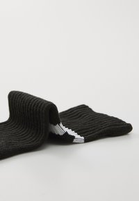 Schwarze, gestrickte Socken mit ribbeliger Textur und einem weißen gestreiften Design am Bündchen. Weicher, flexibler Stoff, am oberen Rand eingekringelt.