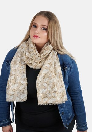 Beige sjaal met bloemmotief en rafelige randen, gemaakt van lichte stof, gedragen over een zwarte top en een spijkerjack.