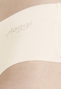 Beige venytetty kangas vyötärö, joka on sileä; sisältää logon "sloggi" painettuna hillityssä sävyssä.