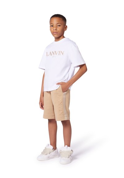 T-shirt blanc à manches courtes avec un logo "LANVIN" beige, associé à un short beige avec un détail de logo sur le côté et des baskets blanches avec des accents texturés.