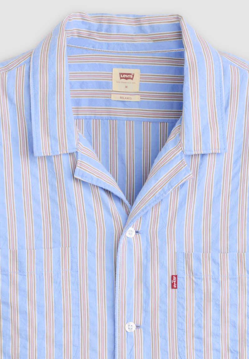 Camisa Levi's de manga corta azul claro con rayas verticales beige, blancas y rojas, corte relajado, cierre de botones y etiqueta roja de Levi's en el bolsillo.