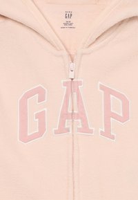 Mjuk rosa baby GAP fleece-huvtröja med framtida dragkedja och "GAP"-logotyp i stora rosa bokstäver omgivna av vitt. Storleksetikett synlig inuti kragen.