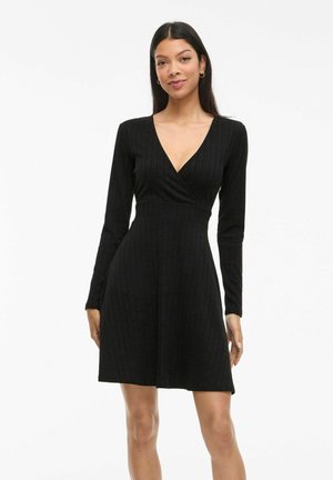 Robe noire côtelée avec des manches longues, décolleté en V, taille cintrée et jupe évasée. Fabriquée en tissu tricoté texturé, idéale pour un style décontracté.